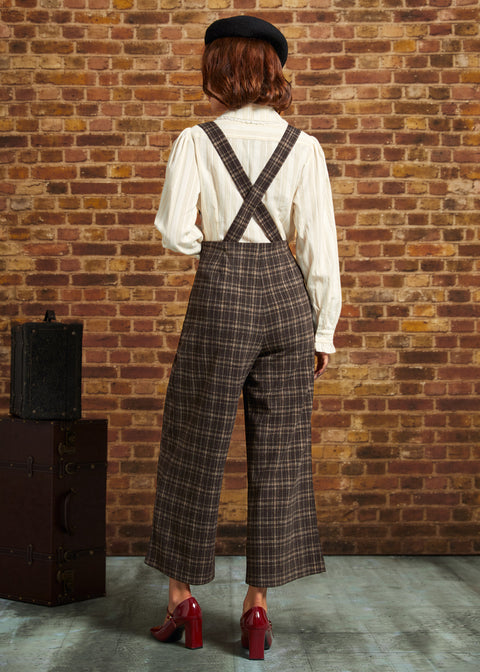 Back view of woman wearing brown plaid cropped pants with suspender straps crossed at the back