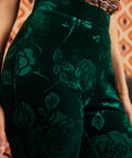 Close-up of a person wearing dark green velvet pants with a tonal floral rose pattern, paired with a striped top.