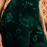 Close-up of a person wearing dark green velvet pants with a tonal floral rose pattern, paired with a striped top.