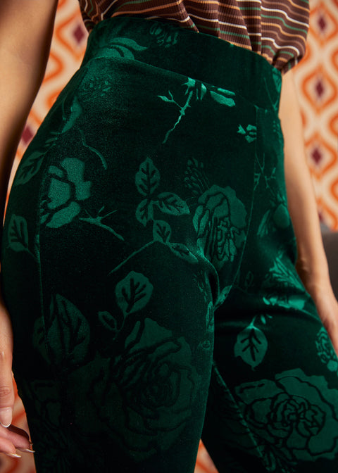 Close-up of a person wearing dark green velvet pants with a tonal floral rose pattern, paired with a striped top.