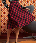 A woman twirling in a ModCloth red and black buffalo plaid A-line skirt, paired with a black and white patterned long-sleeve sweater and black-and-white vintage inspired shoes.