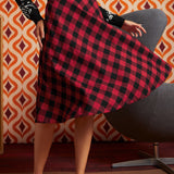 A woman twirling in a ModCloth red and black buffalo plaid A-line skirt, paired with a black and white patterned long-sleeve sweater and black-and-white vintage inspired shoes.