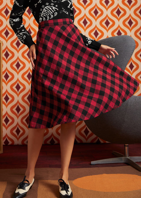 A woman twirling in a ModCloth red and black buffalo plaid A-line skirt, paired with a black and white patterned long-sleeve sweater and black-and-white vintage inspired shoes.