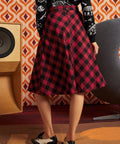Woman wearing red and black buffalo check midi skirt with black dinosaur cardigan and oxford shoes, back view showing full A-line silhouette and center-back zipper