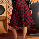 Woman wearing red and black buffalo check midi skirt with black dinosaur cardigan and oxford shoes, back view showing full A-line silhouette and center-back zipper