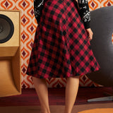 Woman wearing red and black buffalo check midi skirt with black dinosaur cardigan and oxford shoes, back view showing full A-line silhouette and center-back zipper