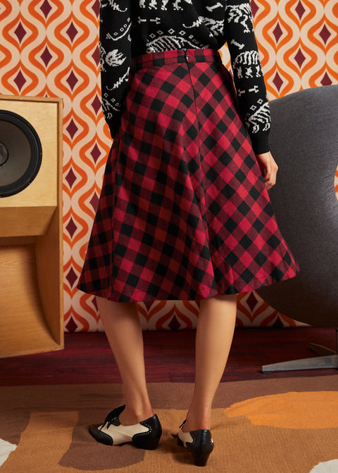 Woman wearing red and black buffalo check midi skirt with black dinosaur cardigan and oxford shoes, back view showing full A-line silhouette and center-back zipper
