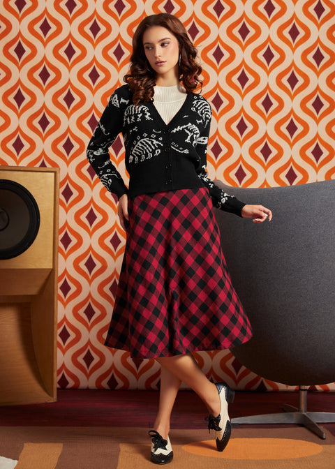 A woman models a black dinosaur bones cardigan and a red and black buffalo plaid midi skirt from ModCloth