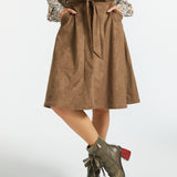 A brown A-line skirt with a matching fabric tie belt and side pockets, styled with a patterned blouse and lace-up ankle boots on a light gray studio background.