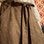 Close-up of the removable self-tie belt on a mocha brown A-line skirt, highlighting the subtle swirling floral pattern and soft suede-like texture.