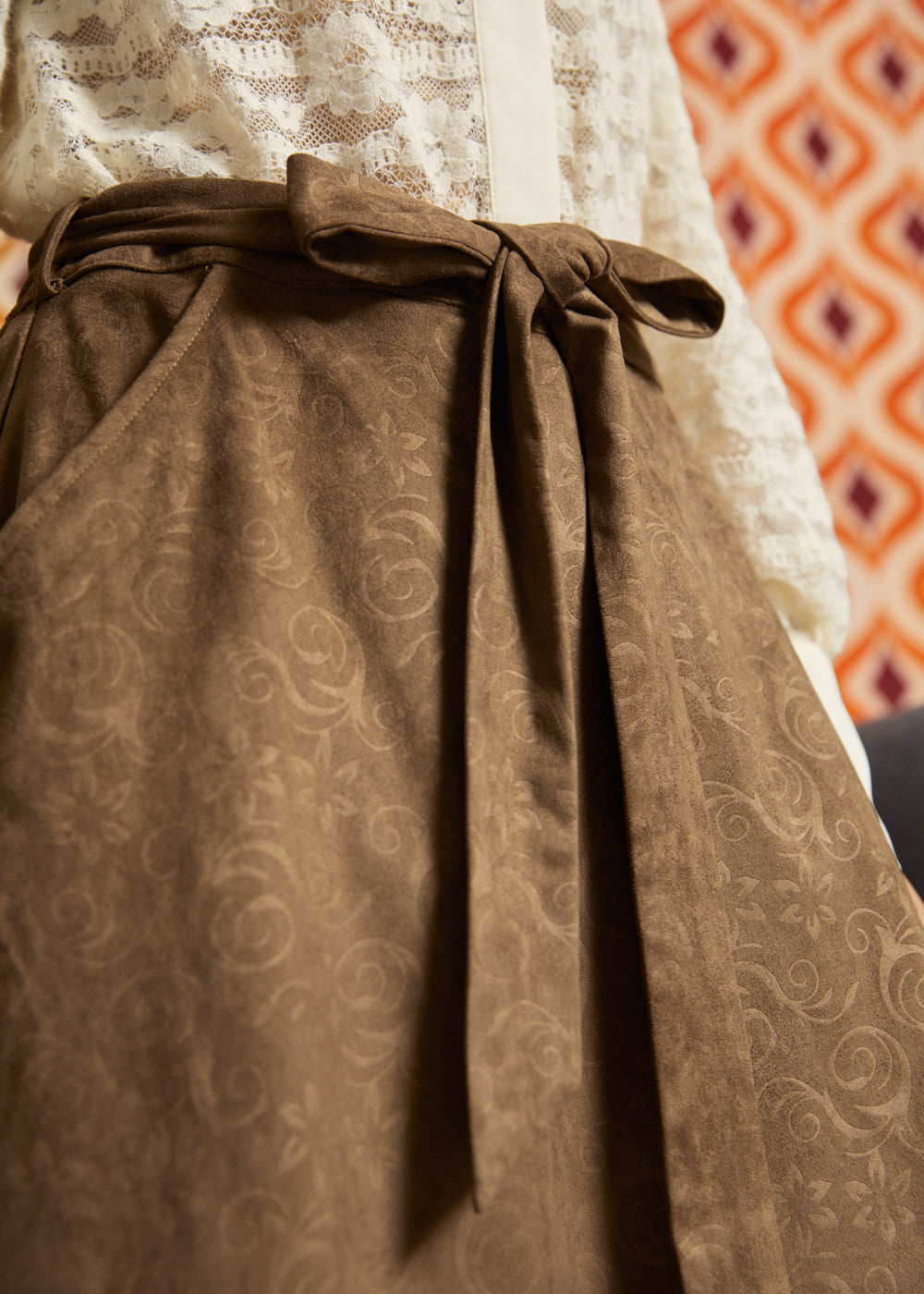 Close-up of the removable self-tie belt on a mocha brown A-line skirt, highlighting the subtle swirling floral pattern and soft suede-like texture.