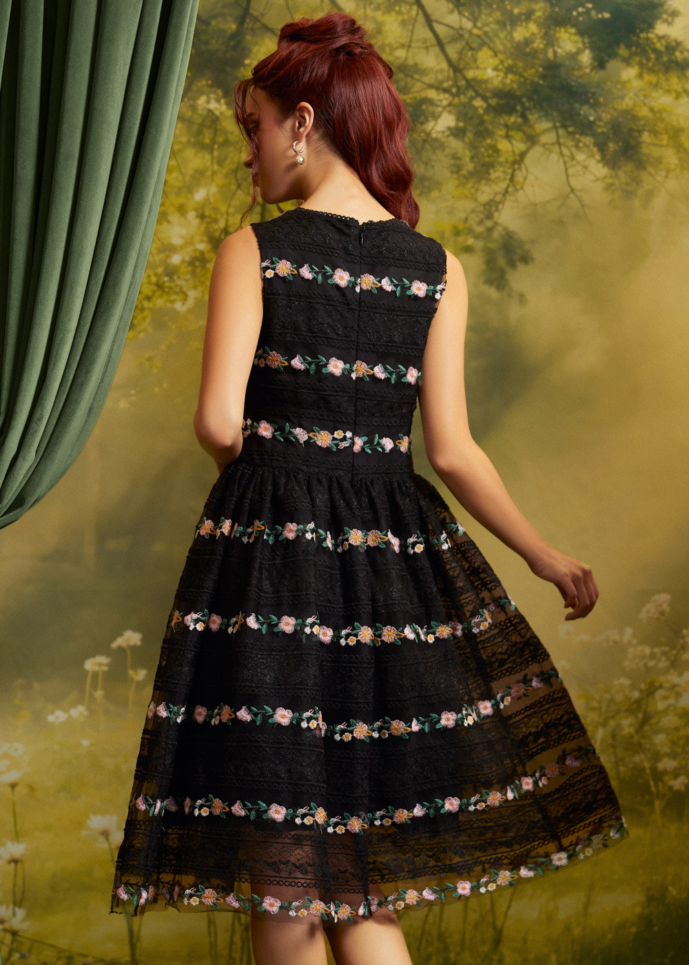 Back view of The Vivienne V-Neck Dress showing colorful floral embroidery in horizontal bands across black lace, a fitted sleeveless bodice, and a full skirt.