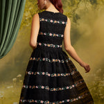 Back view of The Vivienne V-Neck Dress showing colorful floral embroidery in horizontal bands across black lace, a fitted sleeveless bodice, and a full skirt.