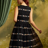 Back view of The Vivienne V-Neck Dress showing colorful floral embroidery in horizontal bands across black lace, a fitted sleeveless bodice, and a full skirt.
