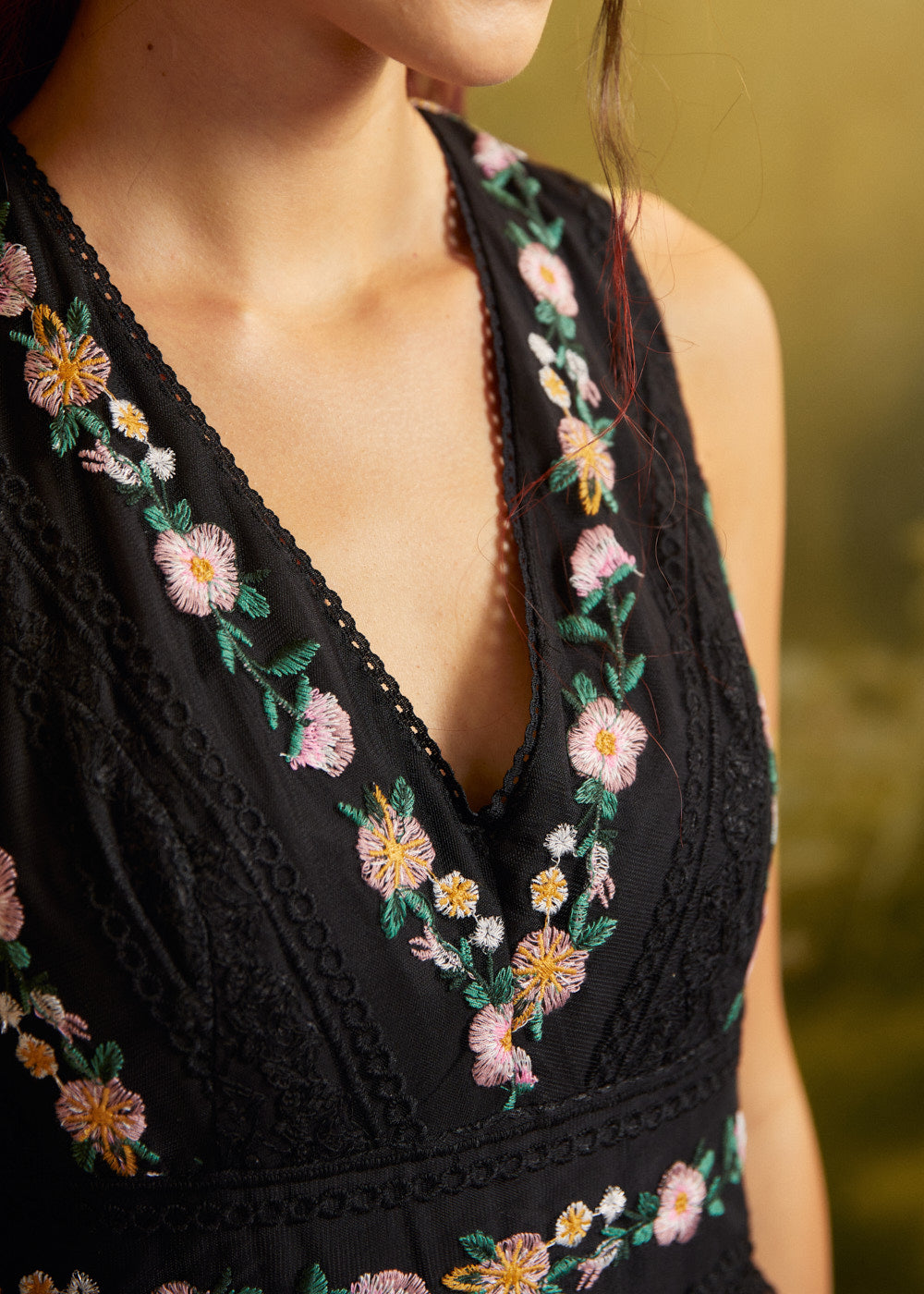 Close-up of the V-neckline on a black special occasion dress with pink and yellow floral embroidery, green leaves, and decorative black lace trim.