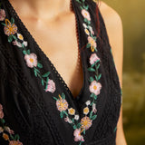 Close-up of the V-neckline on a black special occasion dress with pink and yellow floral embroidery, green leaves, and decorative black lace trim.