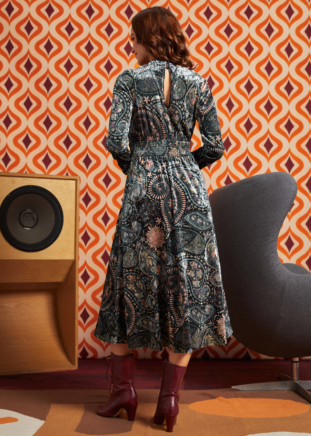 Woman wearing dark paisley floral midi dress with burgundy boots, back view showing keyhole opening, smocked waist, and full midi skirt