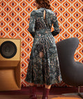 Woman wearing dark paisley floral midi dress with burgundy boots, back view showing keyhole opening, smocked waist, and full midi skirt