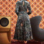 Woman wearing dark paisley floral midi dress with burgundy boots, back view showing keyhole opening, smocked waist, and full midi skirt