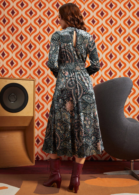 Woman wearing dark paisley floral midi dress with burgundy boots, back view showing keyhole opening, smocked waist, and full midi skirt