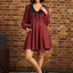 Woman wearing red plaid fit and flare dress with black collar and side pockets, full-length front view