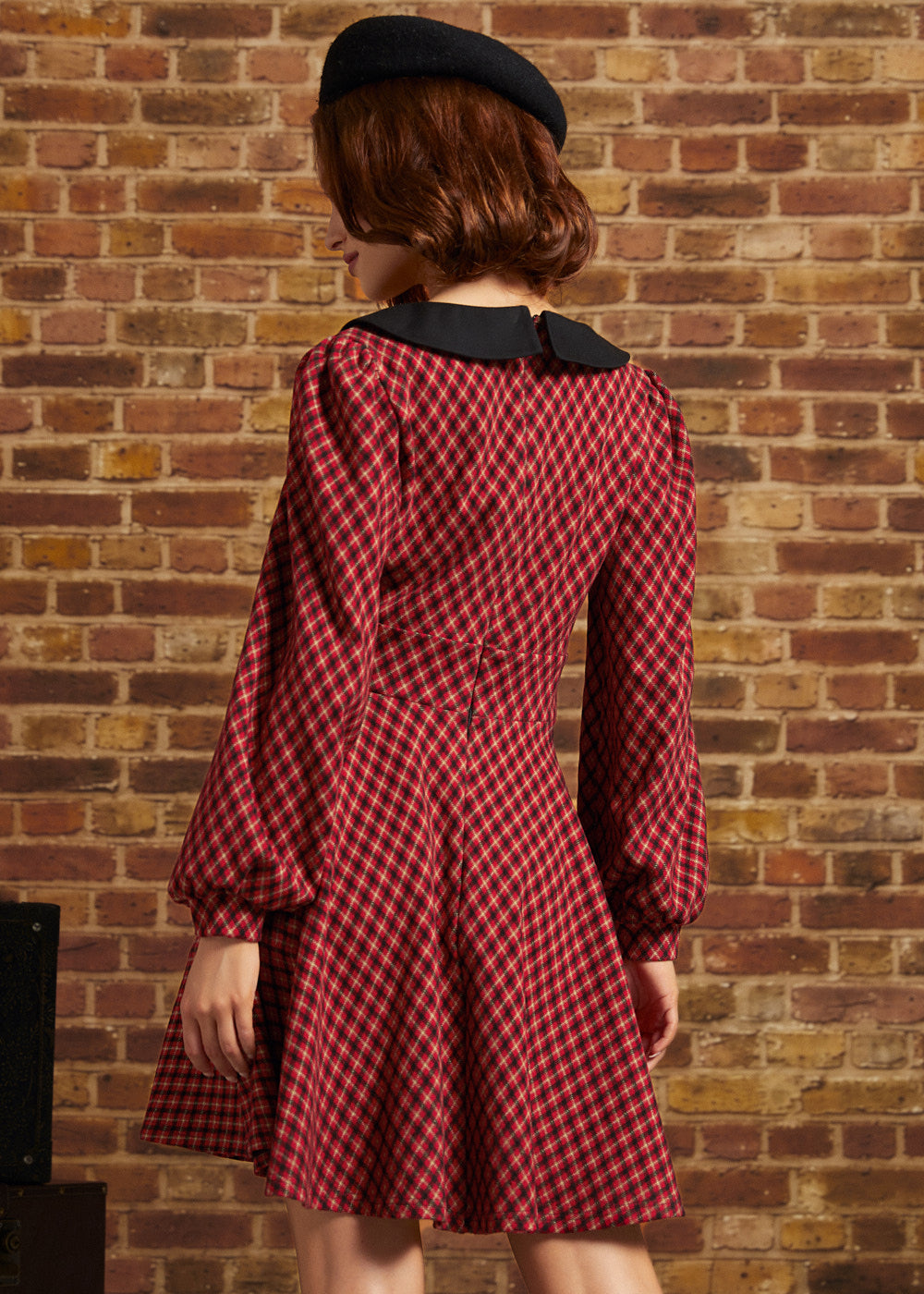 Woman shown from behind wearing red plaid fit and flare dress with long puff sleeves and black collar