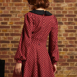 Woman shown from behind wearing red plaid fit and flare dress with long puff sleeves and black collar