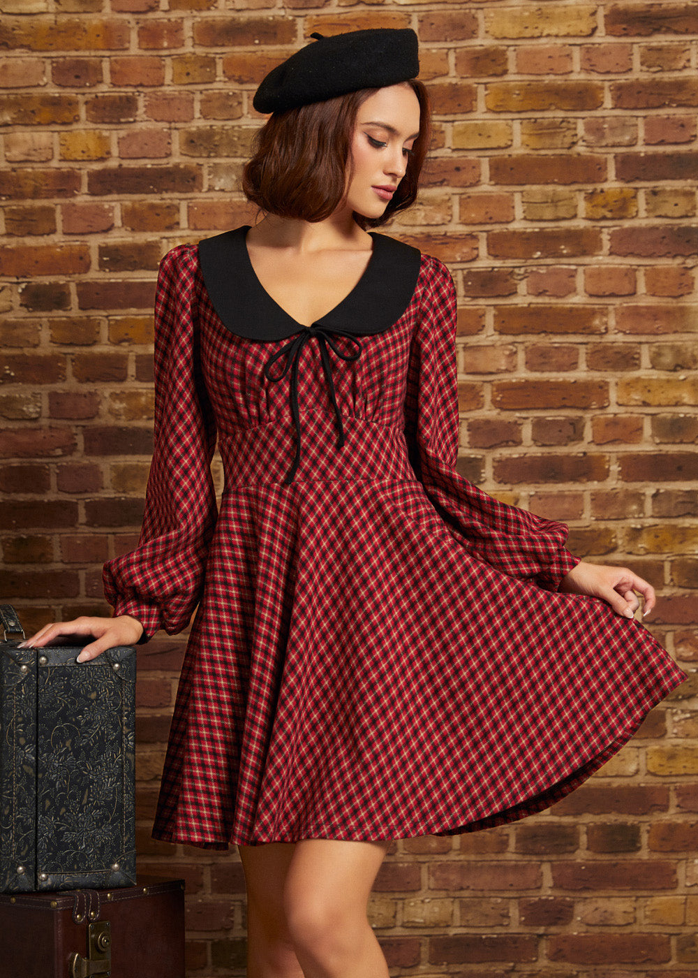 Woman wearing a red plaid fit and flare dress with black contrast collar, tie neckline, long sleeves, and black beret