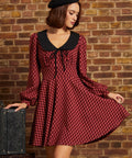 Woman wearing a red plaid fit and flare dress with black contrast collar, tie neckline, long sleeves, and black beret