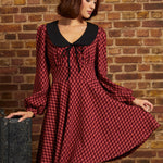 Woman wearing a red plaid fit and flare dress with black contrast collar, tie neckline, long sleeves, and black beret