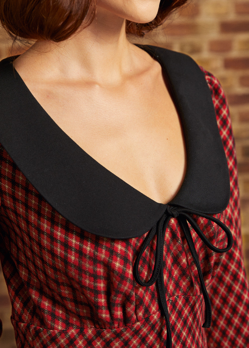 Close-up of oversized black contrast collar and bow tie neckline on red plaid dress