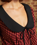 Close-up of oversized black contrast collar and bow tie neckline on red plaid dress