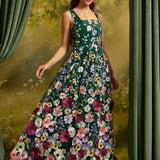 A woman wearing a sleeveless dark green maxi dress covered in colorful floral embroidery, posed in front of a scenic backdrop with green curtains.