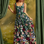 A woman wearing a sleeveless, floor-length floral dress with a dark green base and large multicolored flowers, posed in front of a scenic backdrop with green curtains.