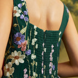 Close-up back view of a dark green sleeveless dress with floral embroidery and a smocked bodice, shown on a model.