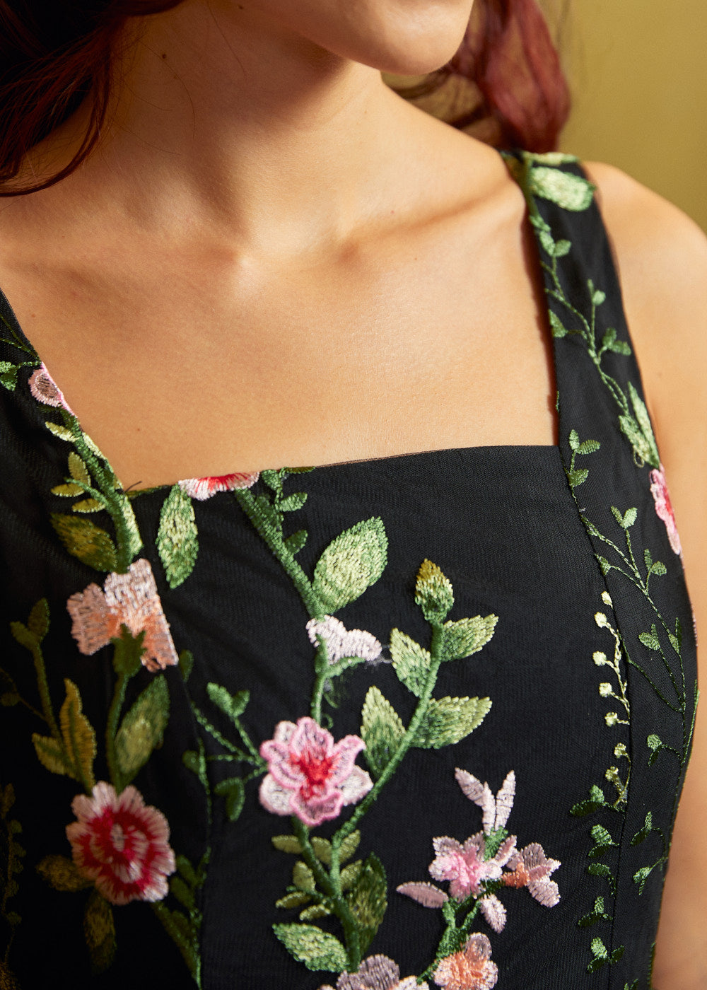 Close-up of a black sleeveless square neck dress bodice with detailed pink and green floral embroidery.