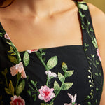 Close-up of a black sleeveless square neck dress bodice with detailed pink and green floral embroidery.