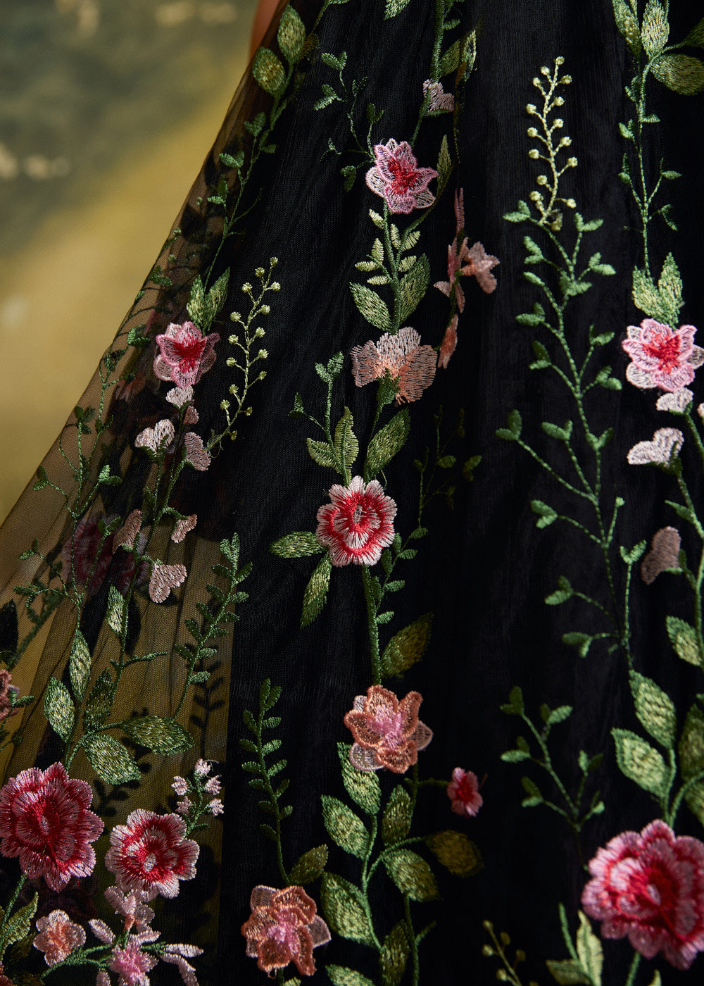 Close-up of a black embroidered skirt with pink and peach flowers and green leaves.