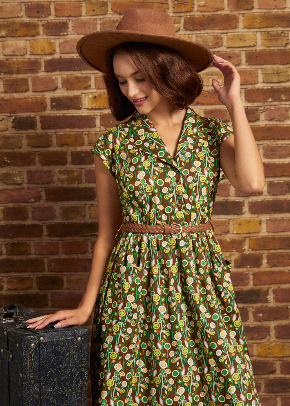 Model in a wide-brim brown hat looking down while wearing the belted floral cotton midi dress, highlighting its retro shirtwaist silhouette and patch pockets.