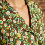 Close-up of the notched collar and button-front bodice with green, cream, and golden yellow circular flowers against a brown background.