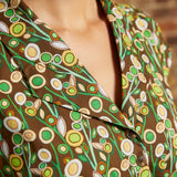 Close-up of the notched collar and button-front bodice with green, cream, and golden yellow circular flowers against a brown background.