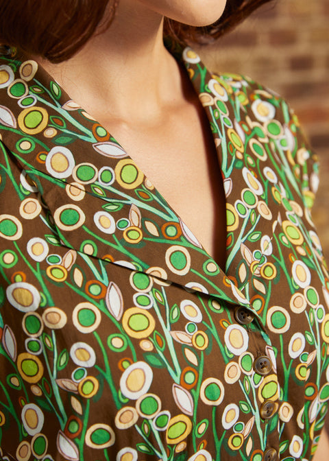 Close-up of the notched collar and button-front bodice with green, cream, and golden yellow circular flowers against a brown background.