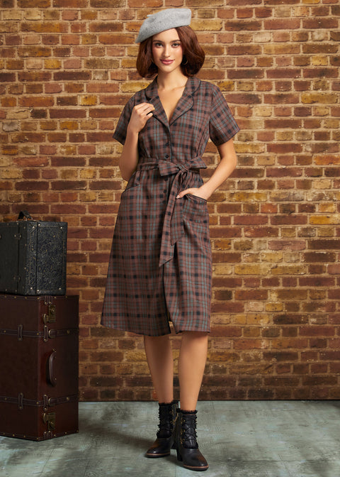 A woman stands in front of a brick wall wearing a short-sleeve plaid wrap dress with a tie waist, a gray beret, and dark lace-up ankle boots. A vintage trunk is visible on the left side of the scene.