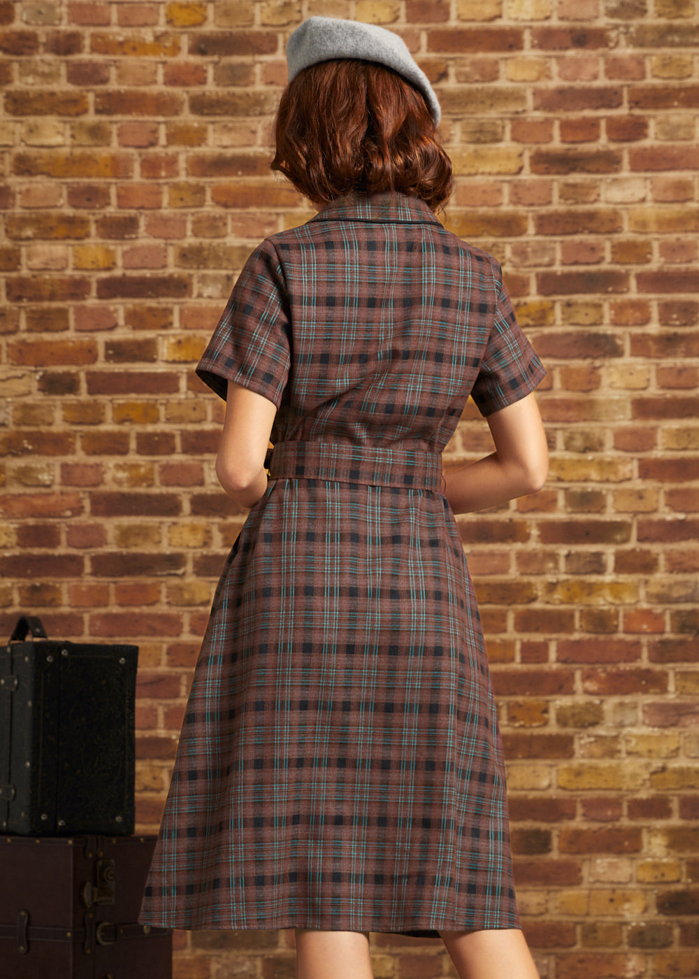 Model wearing a gray beret, photographed from behind in ModCloth's brown plaid Going Out and About Dress with short sleeves, a belted waist, and flared skirt.
