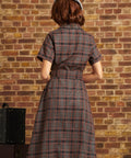 Model wearing a gray beret, photographed from behind in ModCloth's brown plaid Going Out and About Dress with short sleeves, a belted waist, and flared skirt.