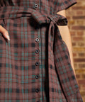 Close-up of the functional black button-front closure, matching plaid self-tie belt, and turquoise-accented brown checked fabric on a vintage inspired dress