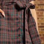 Close-up of the functional black button-front closure, matching plaid self-tie belt, and turquoise-accented brown checked fabric on a vintage inspired dress