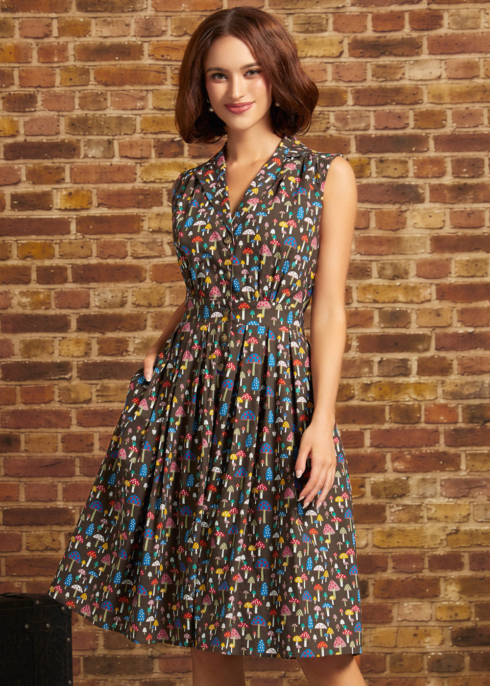 A woman wearing a sleeveless V-neck midi dress with a colorful abstract print, standing in front of a brick wall.