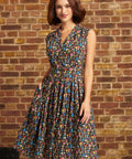 A woman wearing a sleeveless V-neck midi dress with a colorful abstract print, standing in front of a brick wall.