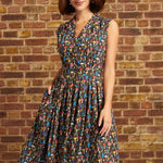 A woman wearing a sleeveless V-neck midi dress with a colorful abstract print, standing in front of a brick wall.
